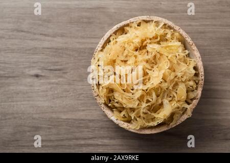 Hochwinkeliger Blick auf eine Steingutschüssel mit gekochtem Sauerkraut, deutsch fein geschnittener fermentierter Kohlkost, auf einer Holzoberfläche Stockfoto
