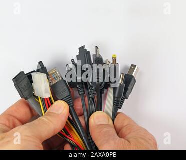 Der Mann hält etwa ein Dutzend verschiedener Stecker für elektronische Geräte in seinen Händen. Stockfoto