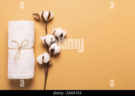Ein sauberes weißes weiches Handtuch wird aufgerollt und mit einem Leinwandseil mit einem Baumwollzweig auf braunem Grund gefesselt. Das Konzept der Reinheit und Natürlichkeit. S Stockfoto