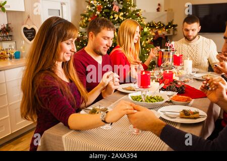 Freunde, die sich die Hände halten und zu Hause beim Weihnachtsessen beten Stockfoto