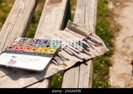 Kunstpalette, Aquarelle, Bürsten auf einer Holzbank im Freien Stockfoto