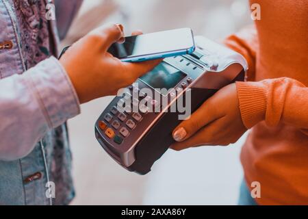 Weibliche Kunden, die das Telefon in der Nähe des nfc-Terminals halten, zahlen kontaktlose mobile Geräte Stockfoto