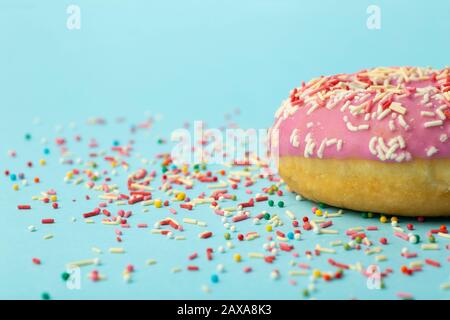 Donut (Donut) in verschiedenen Farben auf blauem Grund mit mehrfarbigen festlichen Zuckerstreuen. Urlaub und Süßigkeiten, Backen für Kinder, Zucker c Stockfoto