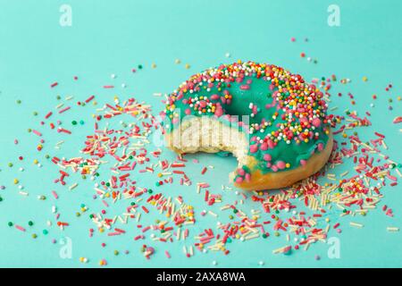 Donut (Donut) in verschiedenen Farben auf grünem Hintergrund mit mehrfarbigen festlichen Zuckerstreuen. Urlaub und Süßigkeiten, Backen für Kinder, Zucker Stockfoto