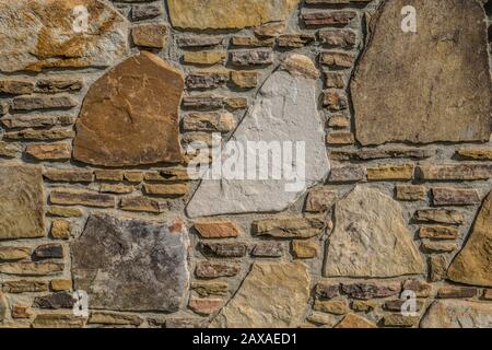 Verschiedene Steine mit verschiedenen Formen, die an einem sonnigen Tag zwischen Mörtel für eine Wand eines Gebäudes im Freien gestapelt sind Stockfoto