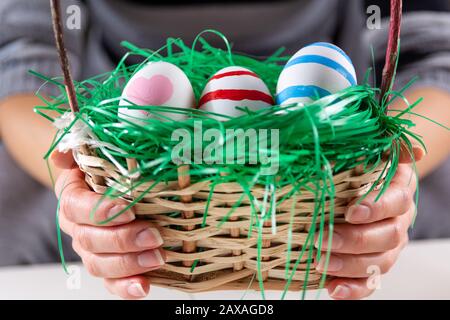 Mädchen übergibt sich mit Ostern bunte Eier in einem Holzkorb mit grünem Gras. Mädchen, die einen Korb mit einer Gruppe von Eiern in den Händen halten Stockfoto
