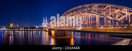 Nachtpanorama der beleuchteten Brücke von der Stadt über den Rhein. Schönes Stadtbild von Köln, Deutschland mit Dom und Großem St. Martin C. Stockfoto