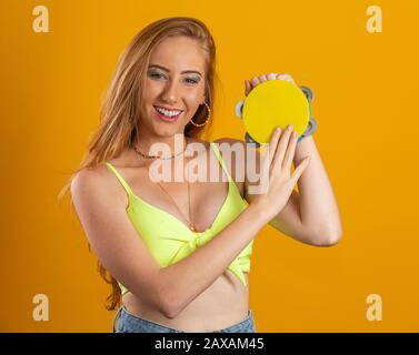 Blonde langhaarige Frau mit einem Spielzeug-Tambourin in den Händen. Auf gelbem Hintergrund. Brasilianerin. Karneval. Rio. Stockfoto