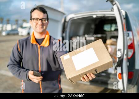 Versandmann hält ein Paket außerhalb seines Autos Stockfoto