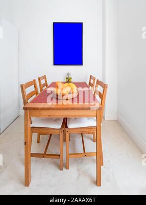 Gemütlicher Holztisch mit Stühlen, Bilderrahmen in einer geräumigen, modernen Küche. Stockfoto