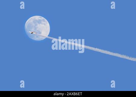 Kommerzielle Flugzeuge/Passagierflugzeug, die in der Dämmerung vor dem Vollmond fliegen und dabei Kondensstreifen/Kondensstreifen zeigen Stockfoto