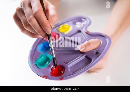 Pinsel in weiblichen Künstlerhands Mischen von Farben auf einer Palette. Mädchen mit Kunststoff-Palette mit verschiedenen Farben und Mischen. Kunst- und Malkonzept Stockfoto