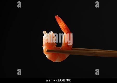 Essstäbchen mit Garnelen auf schwarzem Hintergrund, Nahaufnahme Stockfoto