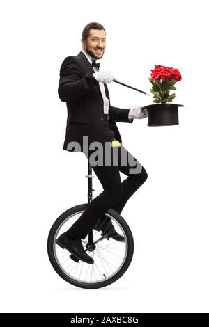 Magier, der mit Zauberstab, Hut und roten Rosen auf einem Einrad reitet und die auf weißem Hintergrund isolierte Kamera betrachtet Stockfoto