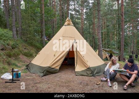 Männer und Frauen lesen eine Karte vor ihrem wigwam geformten Zelt auf dem Waldcamping Stockfoto