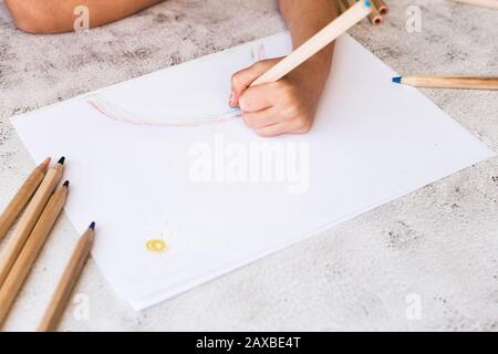 Die Hände des Kindes sind auf einem weißen Papier auf einem grauen Tisch mit farbigen Bleistiften bemalt. Stockfoto