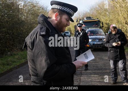 Denham, Großbritannien. Februar 2020. Ein Thames Valley Polizist liest aus einem Buch mit dem Titel "Antiterrorpolicing", während er einem Umweltaktivisten vor Dem Extinction Rebellion eine Warnung ausgibt, der vor einem HGV, der einen JCB-Gabelstapler an einen HS2-Standort liefert, "zu Fuß Unterwegs" gewesen war. Der Aktivist wurde daraufhin verhaftet. Credit: Mark Kerrison/Alamy Live News Stockfoto