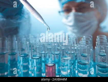 Laborpipette in der Hand eines Arztes, die Flüssigkeit in ein Reagenzglas tropft. Stockfoto