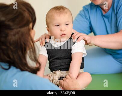 Portrait eines Babys mit zerebraler Lähmung zur Physiotherapie in einem Kindertherapiezentrum. Junge mit Behinderung, der Übungen mit Physiotherapeuten macht. Stockfoto