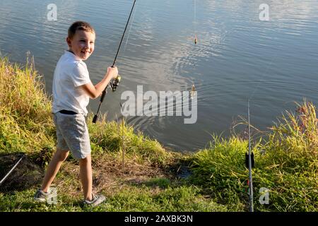 Glücklicher Junge fing einen Fisch. Junge angeln auf einem See. Kind, das Angelrute hält. Kleiner Fischer. Stockfoto