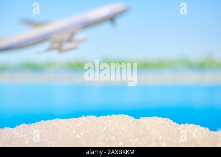 Abstrakter Strand - Sand und Meer als Hintergrund mit fliegendem Flugzeug. Urlaubs- und Reisekonzept. Kopierbereich. Stockfoto