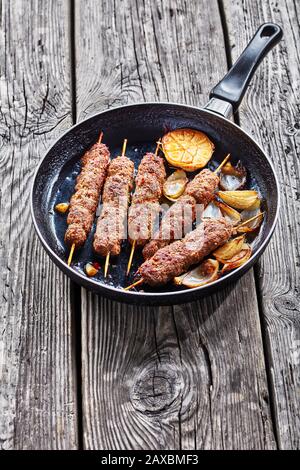 Glutenfreies Rezept für Lammkofta-Kebabs mit traditionellen Gewürzen, die auf Spießen gegrillt werden, serviert auf einer Bratpfanne mit Knoblauch und Zwiebeln, auf dem Hintergrund der BA Stockfoto