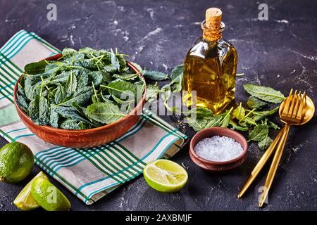 Gesunder Essstil: Frische Kaleblätter auf einer Schüssel, serviert mit Meersalz und Olivenöl, Salatgeschirr und Kalk auf dunklem Betongrund, Horizo Stockfoto