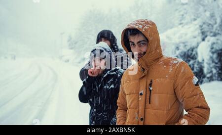 Die kalten Männer warten auf den Bus, während er an einem Wintertag schneit. Transportkonzept im Winter. Stockfoto