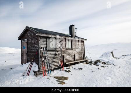 Holzhütte in der Mitte eines verschneiten Berges mit Skier, die darauf lehnen Stockfoto