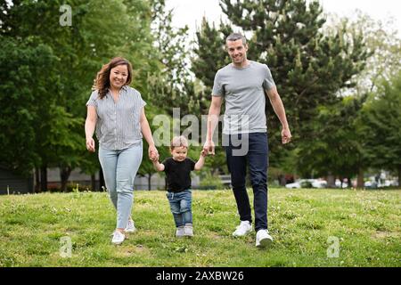 Portrait fröhliche junge Familie, die im Parkgras spazieren geht Stockfoto