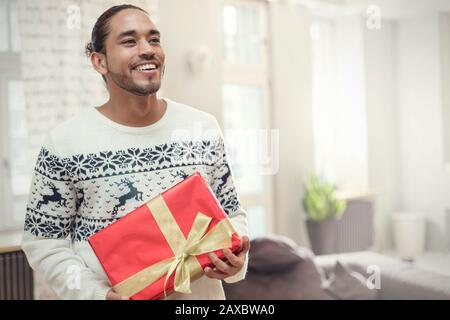Junger Mann im Weihnachts-Pullover mit Geschenk Stockfoto