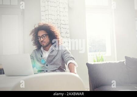 Junger Mann, der am Laptop im sonnigen Wohnzimmer arbeitet Stockfoto