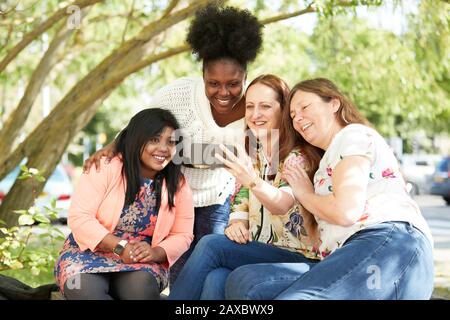 Glückliche weibliche Freunde, die im Park ein Smartphone benutzen Stockfoto