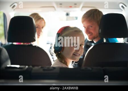 Lächelndes Mädchen im Porträt mit Kopfhörern, die auf dem Rücksitz des Autos fahren Stockfoto