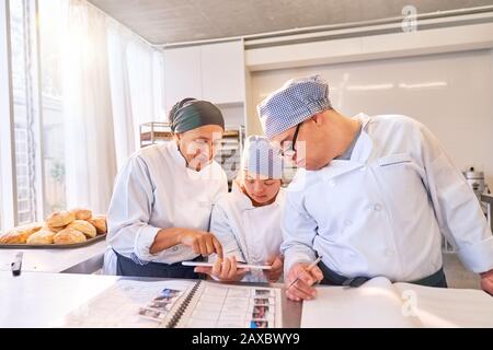 Koch und Studenten mit Down-Syndrom, die digitales Tablet in der Küche verwenden Stockfoto