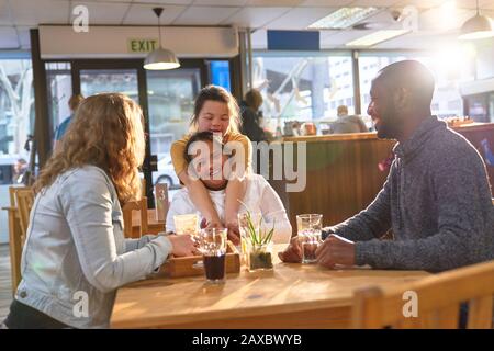 Fröhliche junge Frauen Freunden sich mit Dem Down-Syndrom an, das sich im Café umarmt Stockfoto