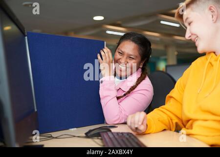 Fröhliche junge Studenten, die am Computer in der Bibliothek lachen Stockfoto