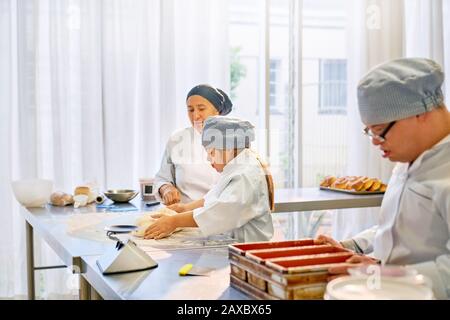 Küchenchef hilft jungen Studentinnen mit Down-Syndrom in der Küche Stockfoto