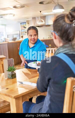 Junger weiblicher Server mit Down-Syndrom, der Essen im Café serviert Stockfoto