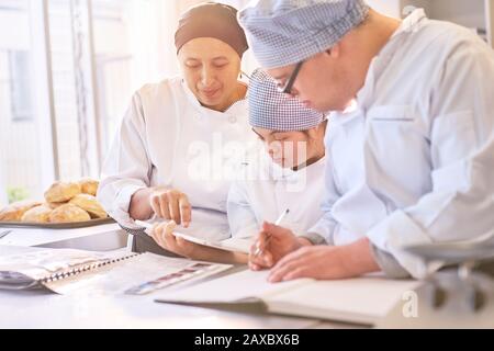 Koch und Studenten mit Down-Syndrom, die Rezepte in der Küche betrachten Stockfoto