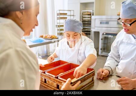 Koch und Studenten mit Down-Syndrom, die Brot in der Küche backen Stockfoto