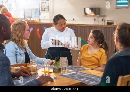 Junger weiblicher Server mit Down-Syndrom, der Ordnung im Café ergreift Stockfoto