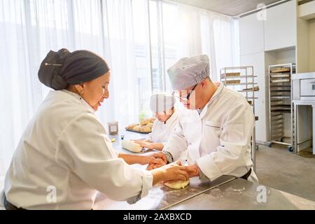 Küchenchef hilft Syndrom-Studenten, Teig in der Küche zu rollen Stockfoto