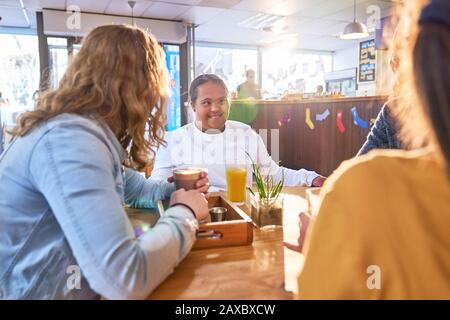 Junge Frau mit Down-Syndrom im sonnigen Café mit Freunden sprechen Stockfoto