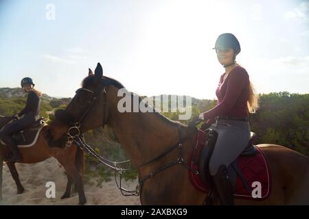 Portrait fröhliche junge Frau, die am sonnigen Strand reitet Stockfoto