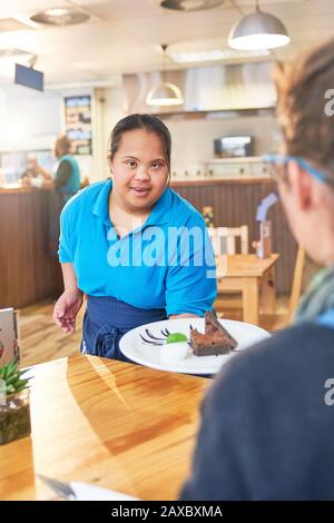 Junger weiblicher Server mit Down-Syndrom, der Dessert im Café serviert Stockfoto