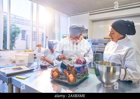 Küchenchef hilft Studenten beim Daen-Syndrom, Muffins in der Küche zu backen Stockfoto