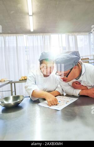 Junge Studenten mit Down-Syndrom, die in der Küche auf Rezept schauen Stockfoto