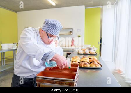 Konzentrierter junger Mann mit Down-Syndrom, der Brot in der Küche backt Stockfoto