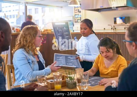 Junges weibliches Server Down Syndrom, das den Kunden im Café Menüs gibt Stockfoto